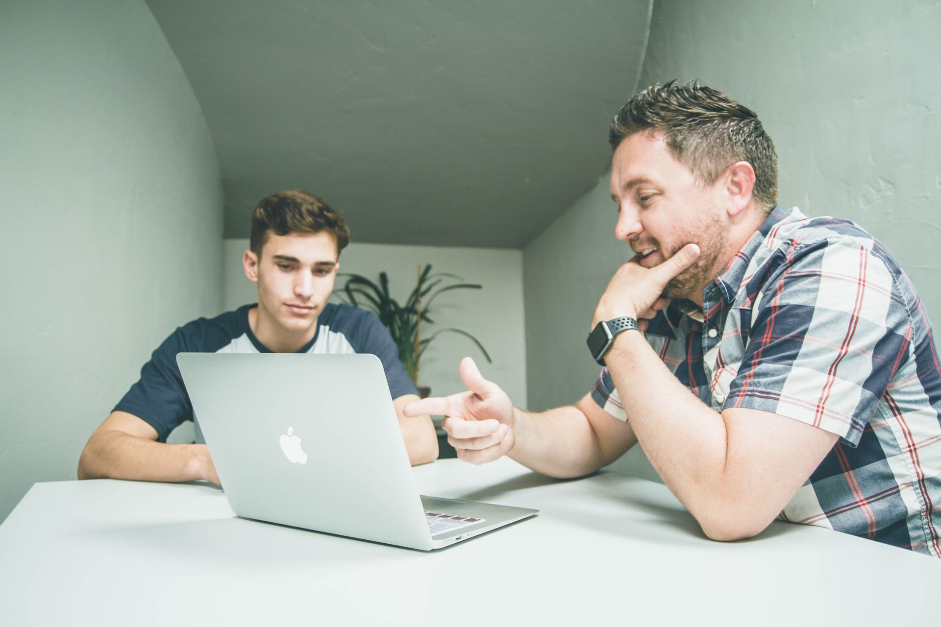 Two men discuss infront of a laptop whilst sat at a table